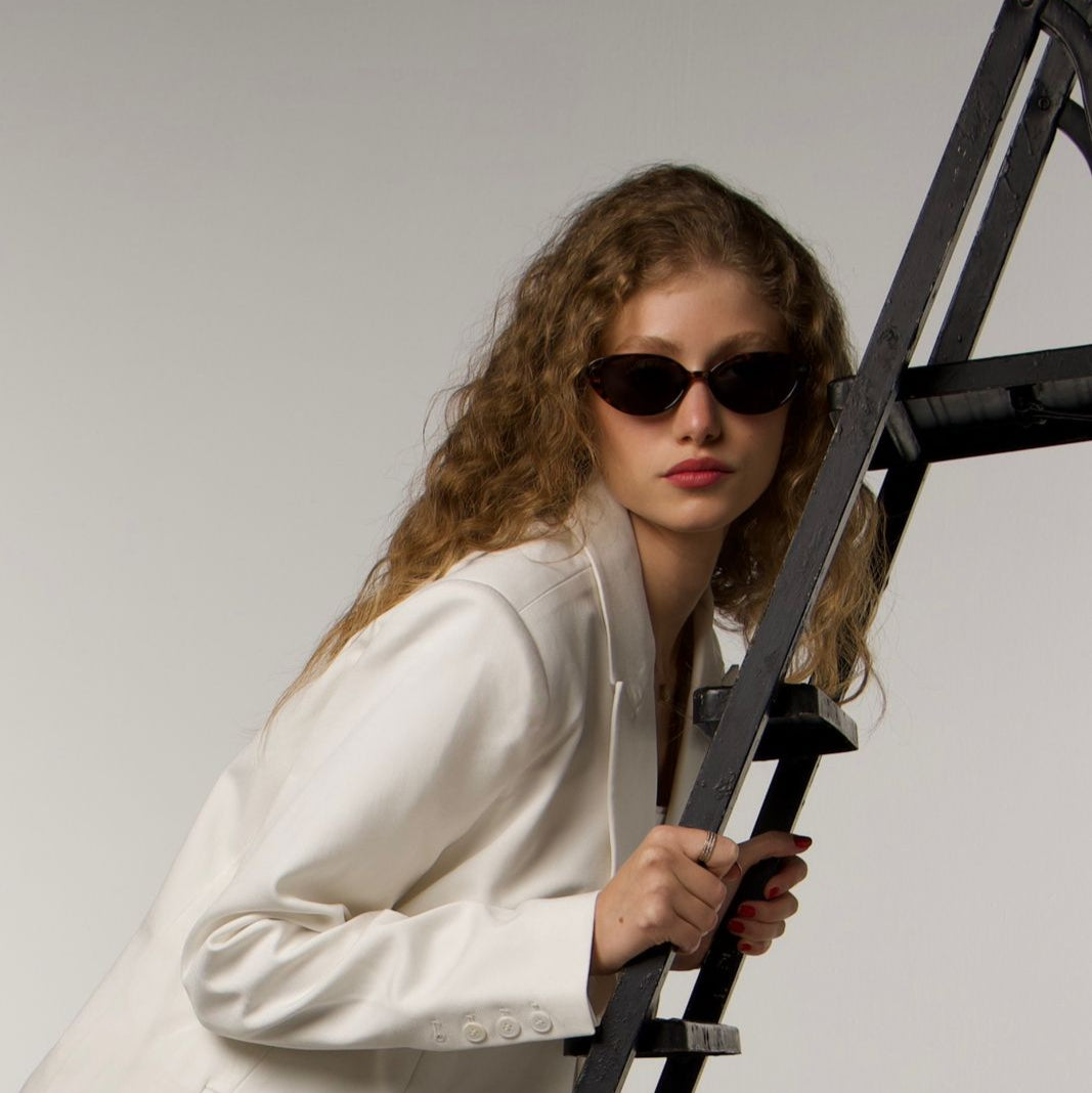 Woman in a white coat holding a black ladder against a plain background